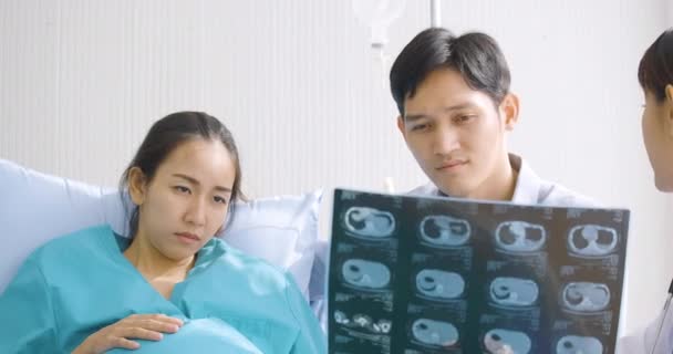 Arzt zeigt schwangeren Frau und ihrem Mann mit ernster Rührung Röntgenergebnisse. — Stockvideo