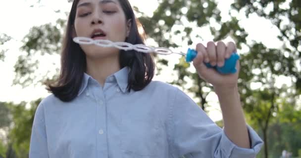 Cámara lenta de sonrisas joven hermosa asiática mujer soplando burbuja al atardecer en el parque . — Vídeo de stock