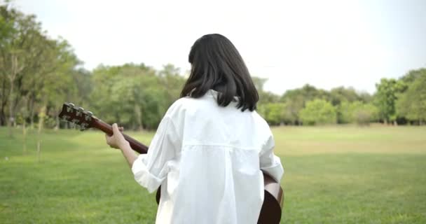 Портрет молодої привабливої азіатки, що грає на акустичній гітарі в літньому парку . — стокове відео