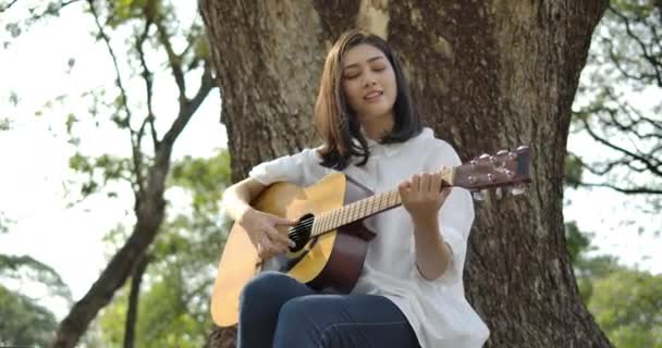 Jonge aantrekkelijke Aziatische vrouw spelen van akoestische gitaar in een zomer-park. — Stockvideo