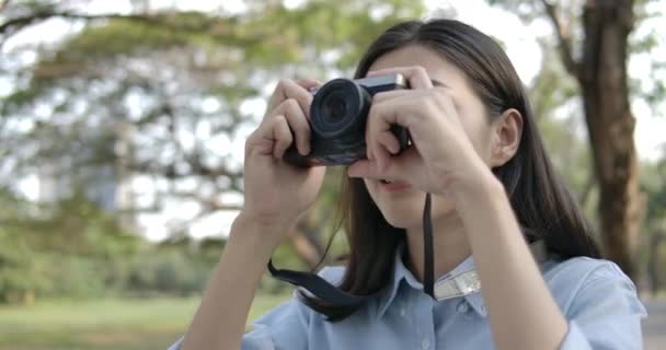 Portrait of young attractive asian woman photographer taking photos in a summer park. — Stock Video