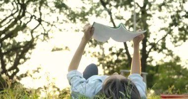 Genç çekici Asyalı kadın günbatımında parkta yeşil çimenlerin üzerinde uzanmış kitap okuma.