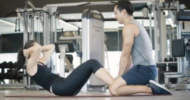 Spor salonunda mekik çeken genç bayanı destekleyen yakışıklı koç..