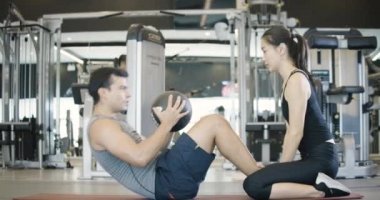 Kafkasyalı genç bir adam spor salonunda kişisel antrenörünün yanında topla mekik çekiyor.. 