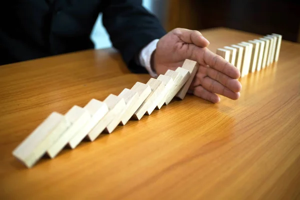 Businessman hand stops domino continuous overturned meaning that hindered business failure. Stop over this business failure concept.