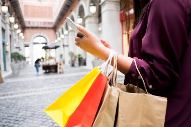 Alışveriş çantası tutan kadın ve alışveriş haftaları için akıllı telefon kullanarak