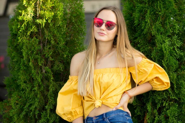 一个漂亮的年轻女子的肖像模特在牛仔裤 黄色上衣和红色的太阳镜微笑着 生活方式的概念 愉快的女孩享受夏天旅行 — 图库照片