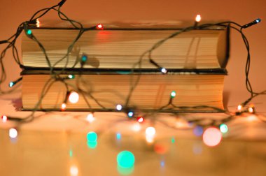 Pembe bir arka plan ve ufuk garland garland ile iki kitap yığını bokeh ön planda ışıklar. Okuma ve eğitim kavramı. Kızlar kavramı için okuma. Noel ve yeni yıl tatilleri için rahat ev iç dekorasyon.