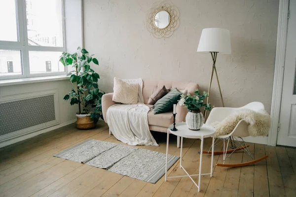 Cozy light interior. Soft beige sofa, white chair, round coffee table, floor lamp, rug and blanket.