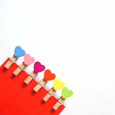 Kırmızı zarf ve beyaz arka planda renkli kalpler ile küçük clothespins. Tatlı aşk. Boşluk Kopyala.