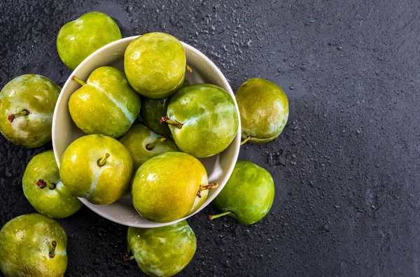 Delicious green plums fresh and raw claudias. On textured background in black color.