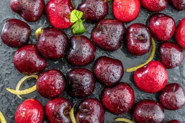 Kıymetli kırmızı ve taze vişneli biralar, dokulu ve damarlı siyah arka planda taze ve çiğ. Limon sarısı lezzet ve nane şekeri yapraklarıyla.