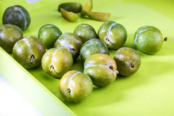 Delicious green plums fresh and raw claudias in wicker basket. On green background color.