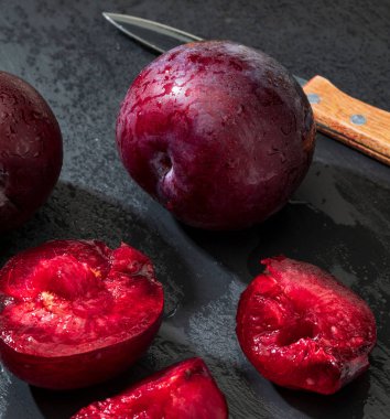 İştah açıcı ve sağlıklı kırmızı erikler, bütün ve siyah bir arka planda kırsal bir görünüm ile bölümlere kesilmiş..