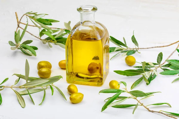 Sızma zeytinyağı cam şişede. Ön plan. Yaprakları ve zeytin dalı içerir. Beyaz dokulu arka plan üzerinde.