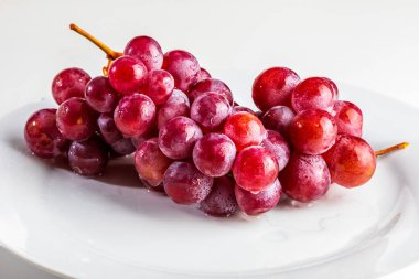 Masanın üzerinde güzel bir kırmızı üzüm kümesi (mürekkep) var. Taze, çiğ ve su damlaları.