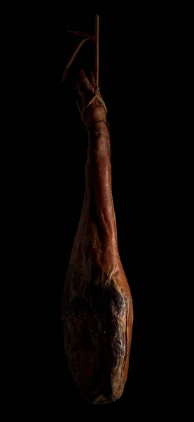 Whole leg of Spanish Iberian serrano ham hanging on a rope. On black background