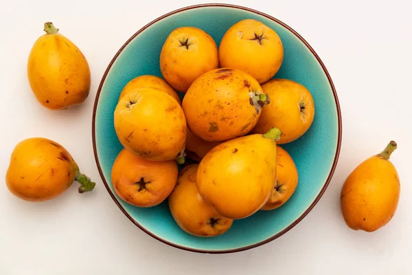 Taze loquats (medlars) mavi turkuaz kase. Beyaz arka planda izole edilmiş. Close-up.Top görünümü.