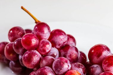 Masanın üzerinde güzel bir kırmızı üzüm kümesi (mürekkep) var. Taze, çiğ ve su damlaları.