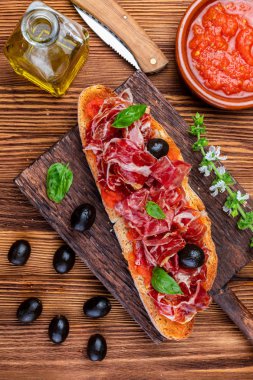 Lezzetli ekmek tost doğal domates, sızma zeytinyağı, İber jambon, siyah zeytin ve fesleğen ile bırakır. Ahşap arka plan üzerinde.