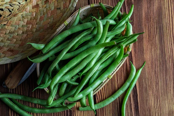 Fresh and raw green beans (green round beans) in wicker basket. Rustic and homemade look on wooden background. Top view.