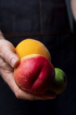 Taze ve çiğ meyve (kırmızı böbrek, şeftali, yeşil armut konferansı) sunan ellerin yakın çekim. Metninizi eklemek için boşlukiçeren koyu arka plan.