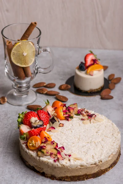 White cake with berries on the table with nuts, cinnamon, a glass, lemon.