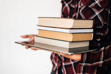 Bir tablet ve kitapların bir yığınına tutan bir kız elleri. Bilgi kavramı.