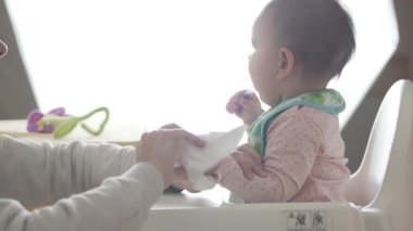 Genç mutlu anne bebeğine kaşıkla ağır çekimde kendi başına yemek yemeyi öğretiyor.