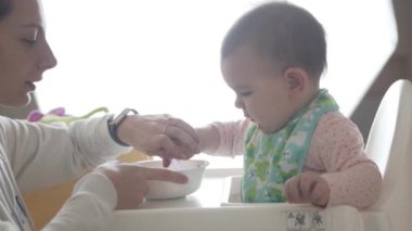 Genç mutlu anne bebeğine kaşıktan, bebek mamasından kendi başına yemeyi öğretiyor.