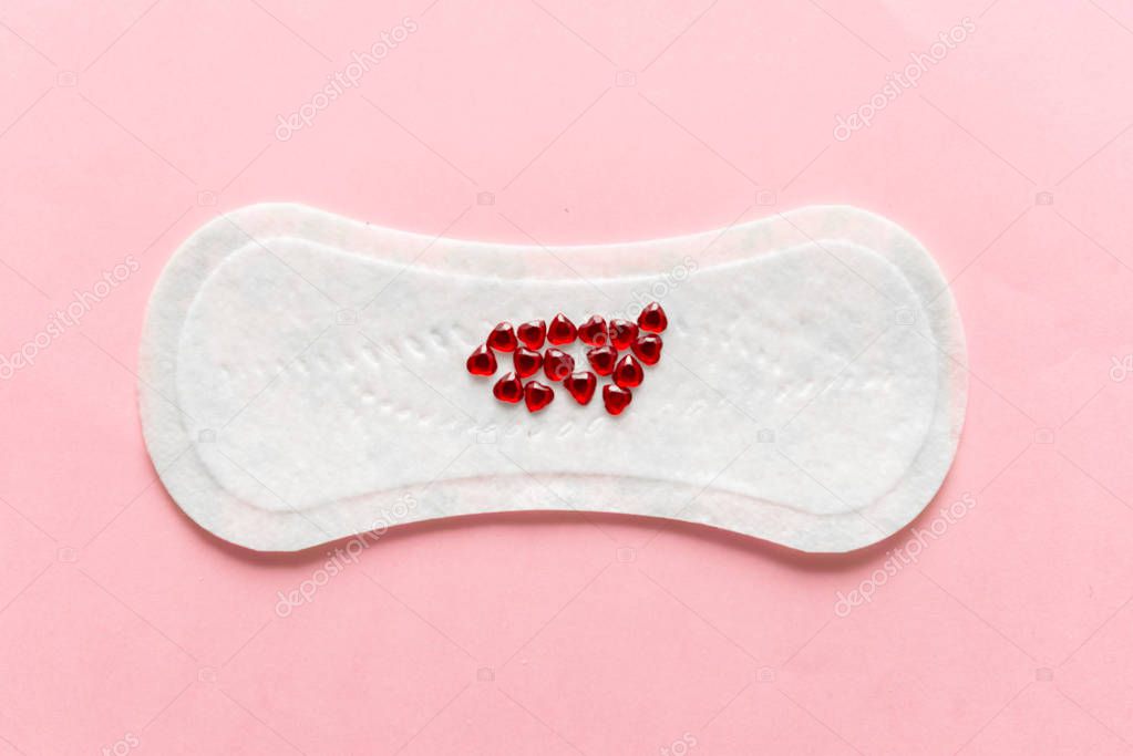 Menstrual pad with red heart glitter on pastel colored background. Minimalist still life