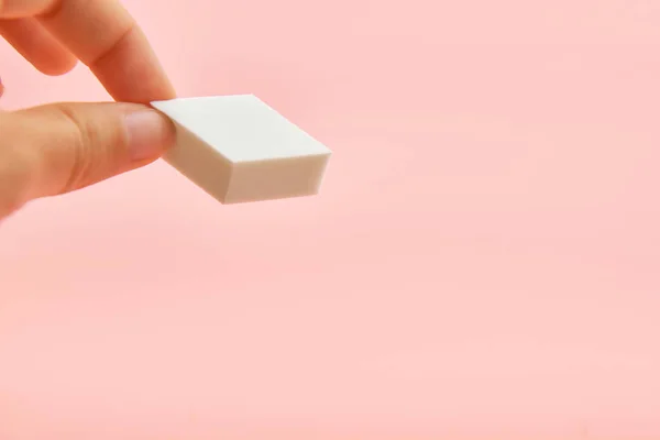 Rectangle cosmetic white sponge in hands on pink background, copy space, beauty