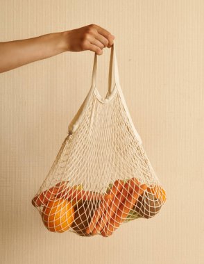 Elinde sebzelerle dolu bir torba tutan kadın. Sıcak toprak tonları olan meyveler, sıfır atık.