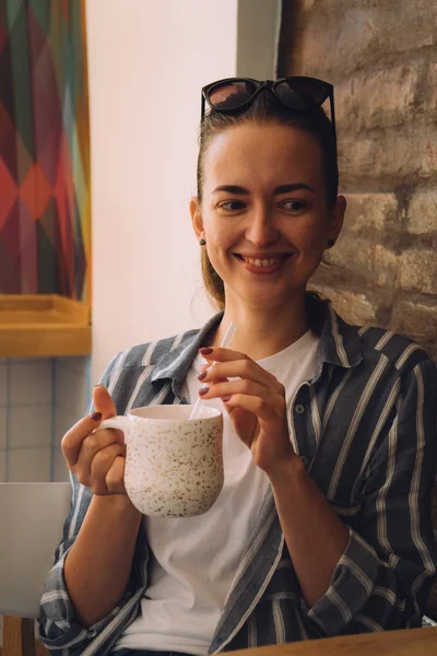 Young pretty woman sitting in a cafe and talking on the phone. The girl drinks hot coffee — Stock Photo, Image