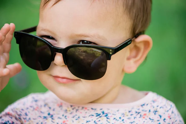 Ребенок в солнцезащитных очках на фоне зеленой травы в солнечный день, образ жизни — стоковое фото