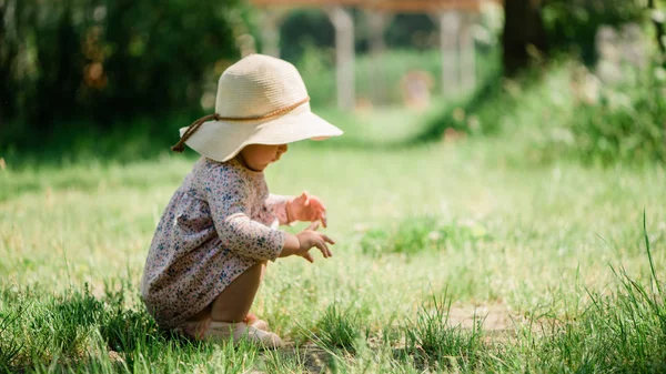 Bebé niña sentada en la hierba - día de verano de la infancia, sombrero de paja, espacio de copia —  Fotos de Stock