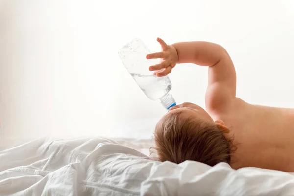 Дитина Тодлер п'є воду з блакитної пластикової пляшки. Сидить на білому тлі. Копіювати простір — стокове фото