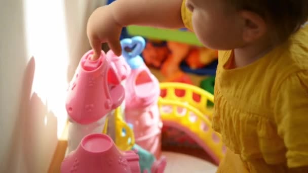 Menina em vestido amarelo senta-se no chão e brinca com brinquedos. Creche ou berçário — Vídeo de Stock