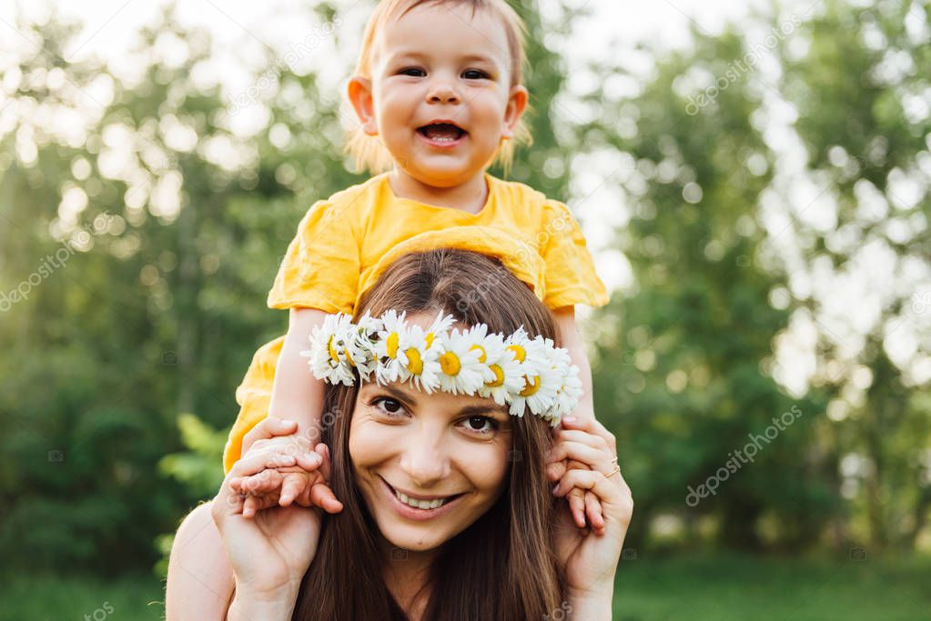 Mother giving piggyback ride to her loving daughter outside in nature. Hippie mother and happy baby concept