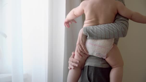 Young mother holding her baby in the bedroom newar the window. Diaper — Stock Video