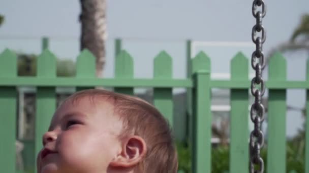 Молода дівчинка-малюк в безпечному гойдалці в літньому саду в жовтій сукні — стокове відео