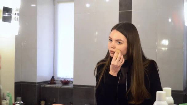 미소와 거울을 보면 얼굴에 화장품 스폰지를 사용하여 아름다운 여자. 4k — 비디오