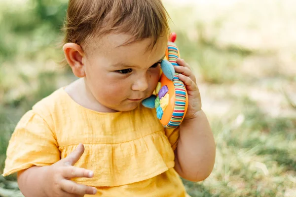 Любопытная маленькая девочка использует игрушечный телефон на открытом воздухе в летний день. Gen z — стоковое фото
