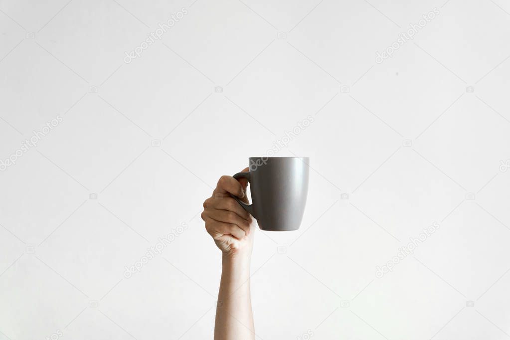 Hand holding a grey cup of coffe om white background. Concept of sleepy morning. Copy space