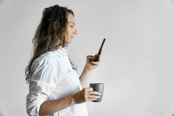 Vacker flicka med vått hår och kopp Coffe textning på smartphone. Kopiera utrymme morgonrutin — Stockfoto