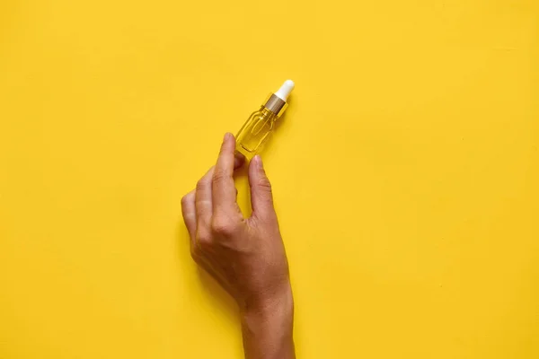 Hand vasthouden ottle met serum of olie van natuurlijke essentie. Gele achtergrond. Minimale — Stockfoto