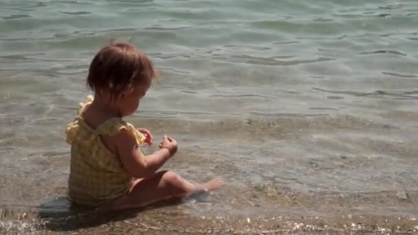 Baby girl in yellow swimsuite plays in water sea. Summertime with toddler on the beach lifestyle — Stock Video