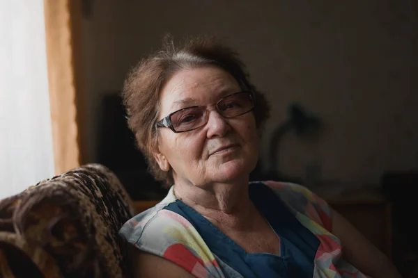 Retrato de una mujer mayor en casa cerca de la ventana. Estilo de vida de la jubilación. Retrato en tonos oscuros —  Fotos de Stock