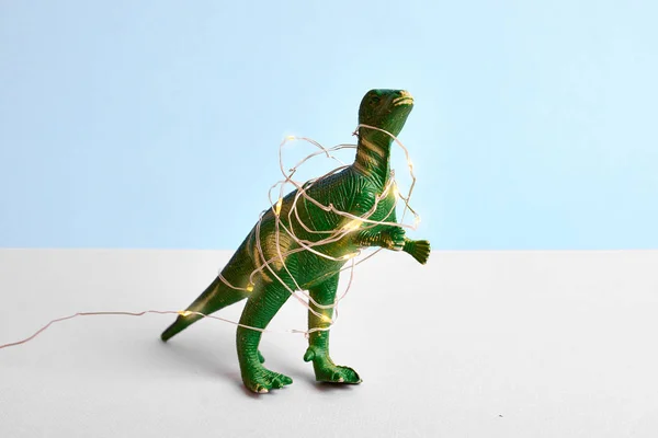 Lustiger grüner Tyrannosaurier-Rex mit rotem Weihnachtsmütze und Weihnachtslicht. Blaues Minimalkonzept — Stockfoto