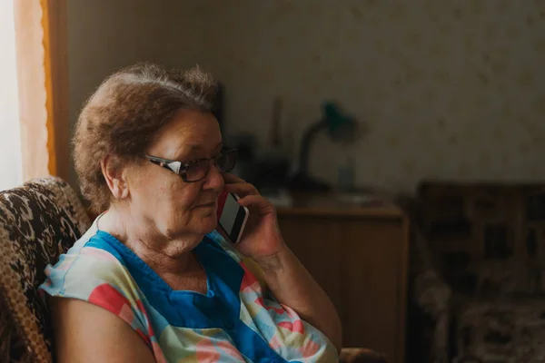 Eine alleinstehende ältere Frau telefoniert am Fenster ihres Wohnzimmers. Kommunikationskonzept — Stockfoto